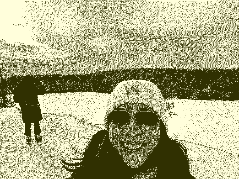 dithered image selfie of a woman wearing a beanie in front of a big lake