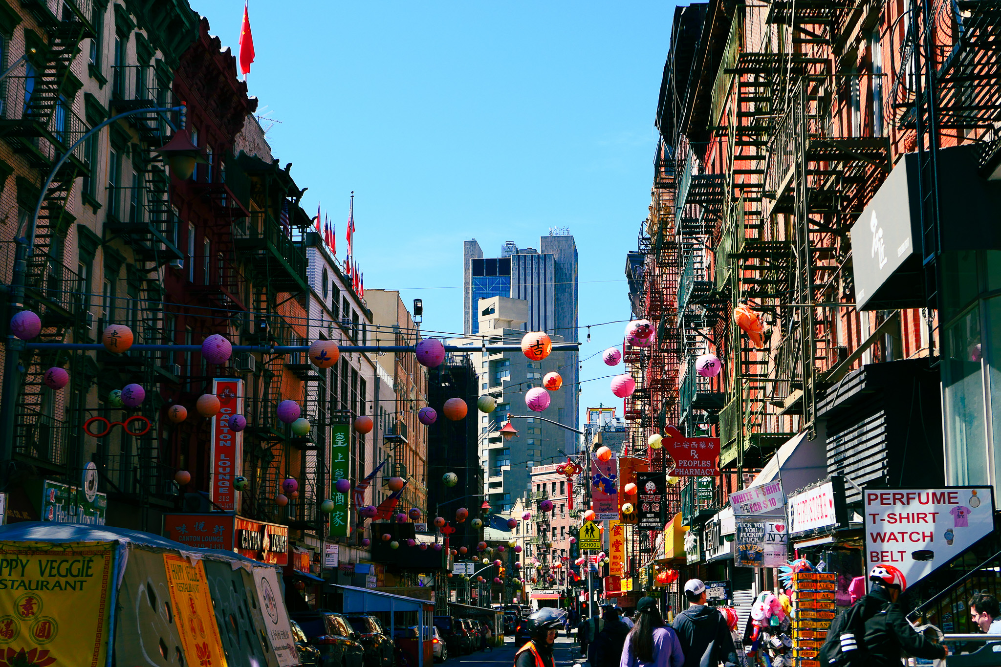 Visually busy shot of Mott Street in Manhattan Chinatown, flanked by rows of buildings with multiple colorful paper lanterns strung between them