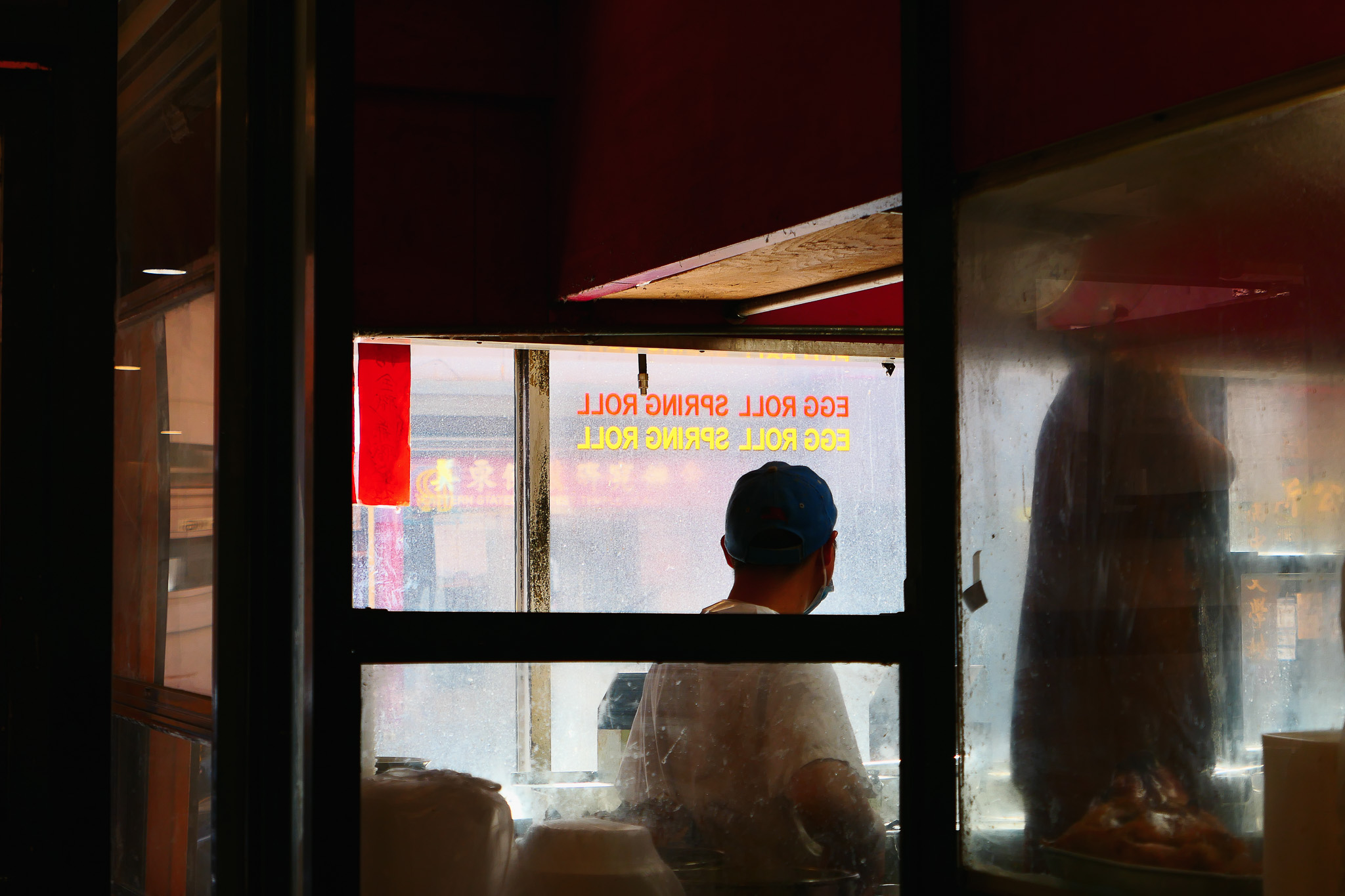 Backlit restaurant worker looks out the window, which has 'egg roll spring roll' lettered on it