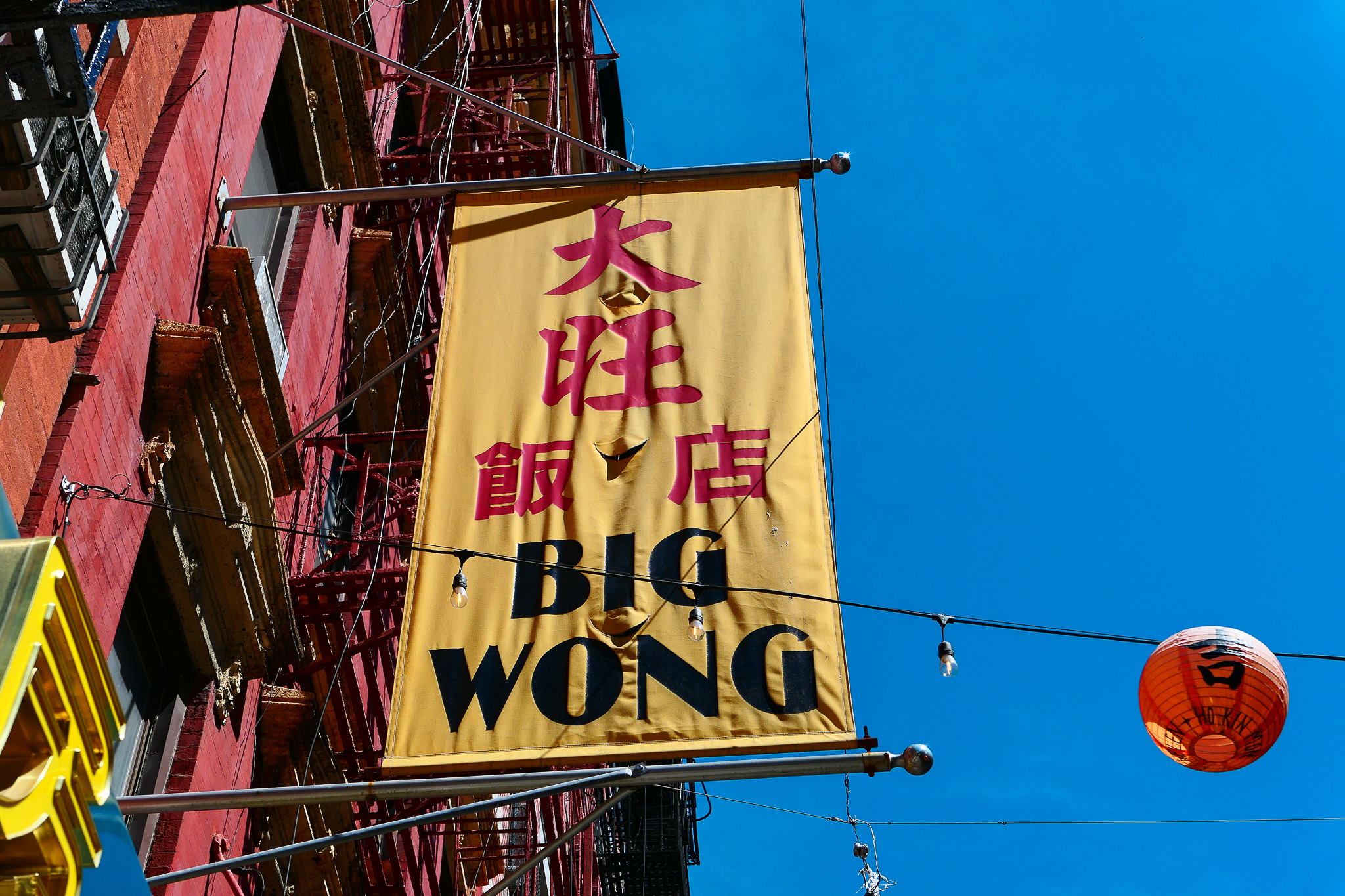 Bright yellow banner with '大旺' and 'Big Wong' on it, longer than it is wide, hanging on the side of a red brick building