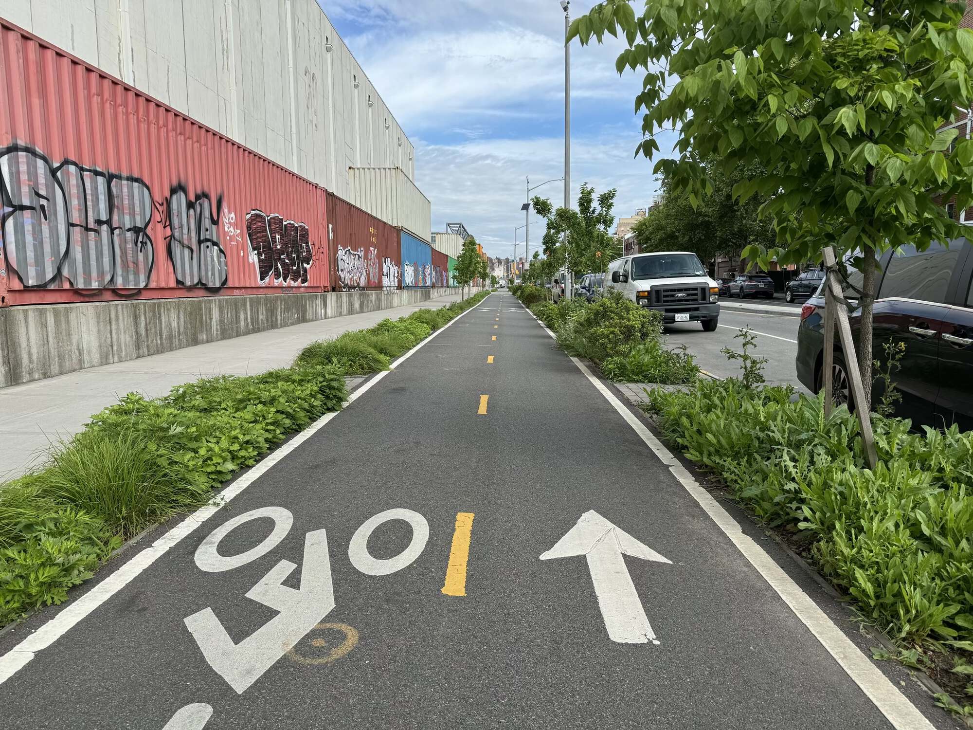 Two-way bicycle path with some light greenery on either side. The sky is blue with many white clouds.